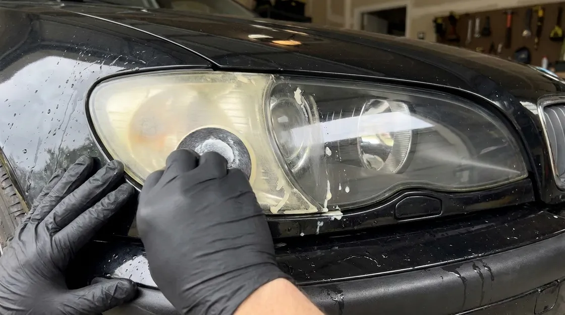 Gloved hands polishing a yellowed headlight back to clear during a restoration