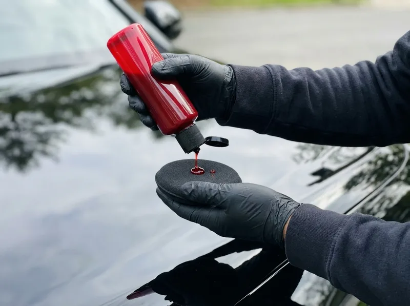 Gloved hands dosing red reactive ceramic sealant onto an applicator pad over a black car